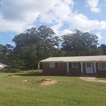 A Brick House With A Metal Roof Is Sitting In The Middle Of A Lush Green Field - Rebecca, GA - Cole and Jones Tree Services