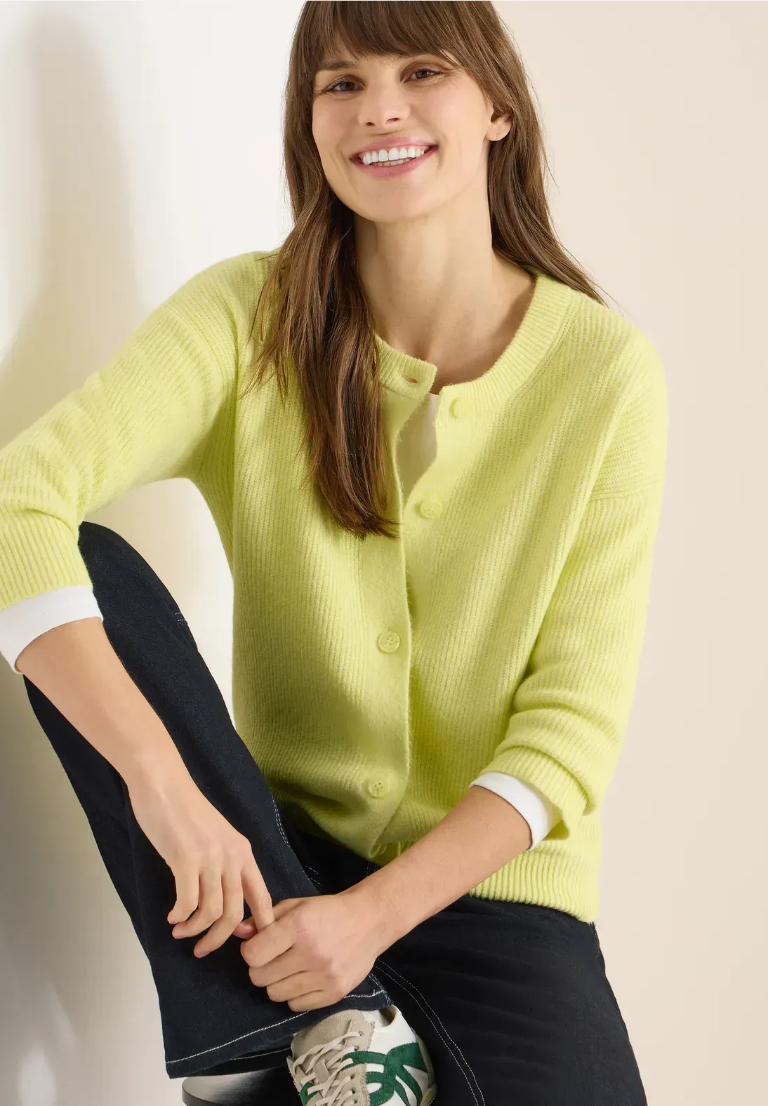 Donna con cardigan verde lime e jeans, sorridente, seduta.
