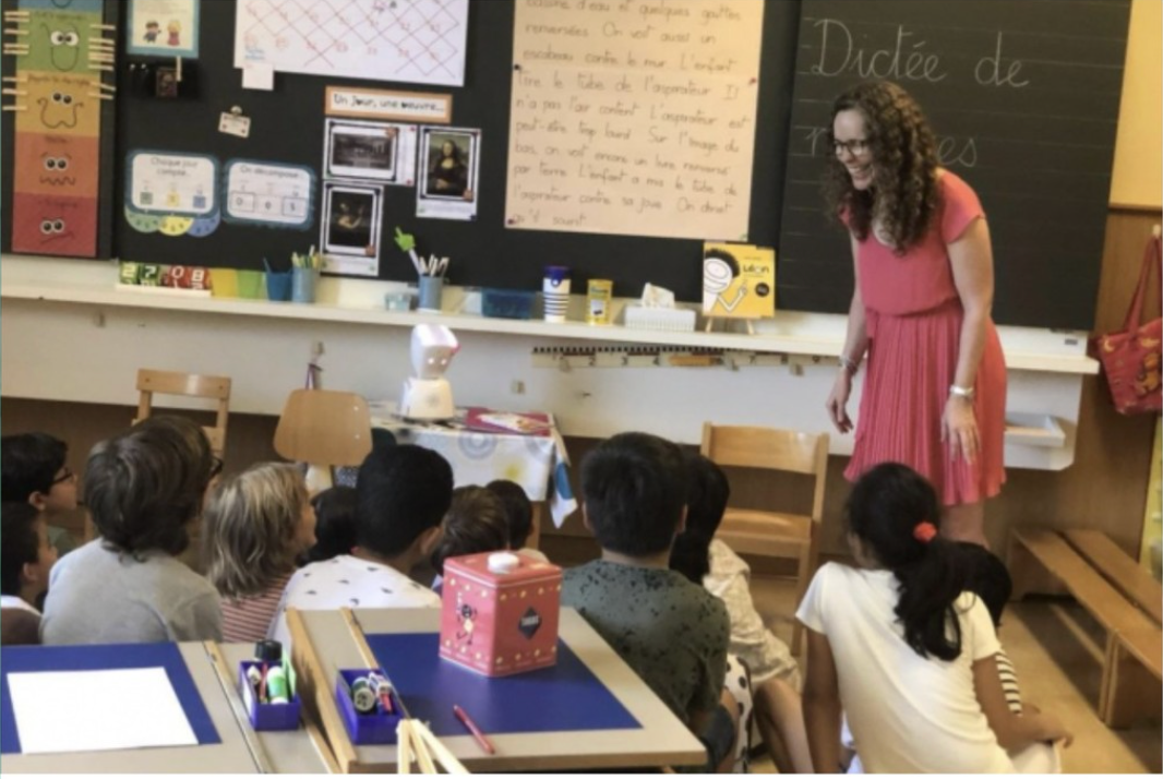 Une femme se tient devant un tableau noir sur lequel est écrit dictee de
