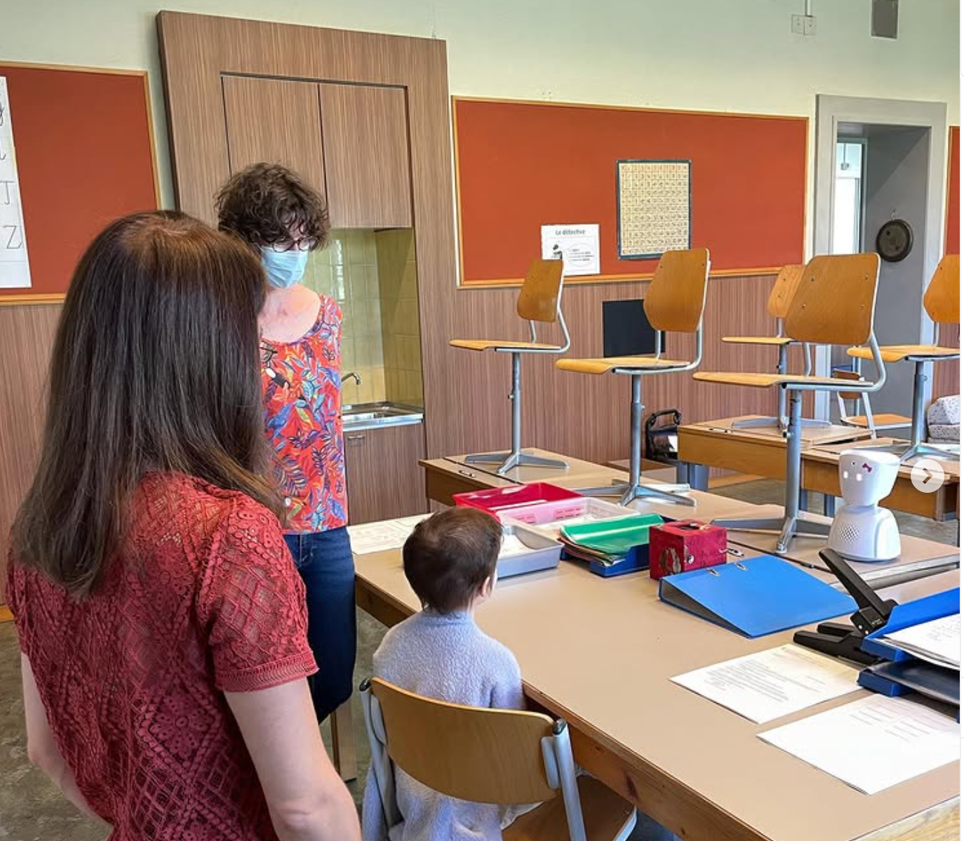 Une femme portant un masque se tient à côté d'un enfant dans une salle de classe