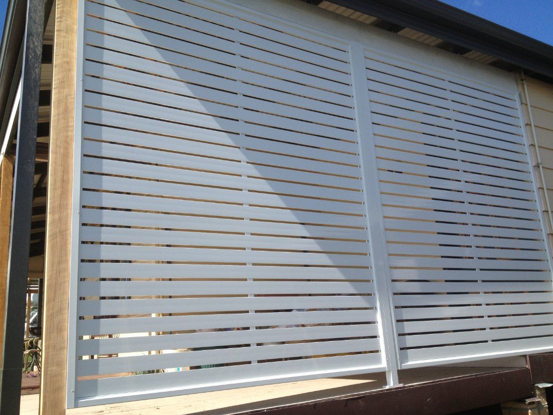 A White Fence is Sitting on the Side of a Building — Newcastle & MidCoast Privacy Screens & Gates In Maitland, NSW