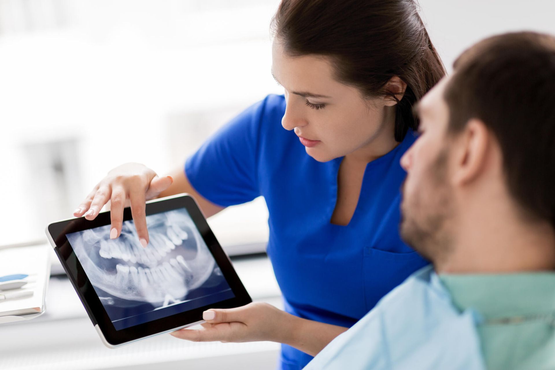 A dentist is looking at an x-ray of a patient 's teeth on a tablet.