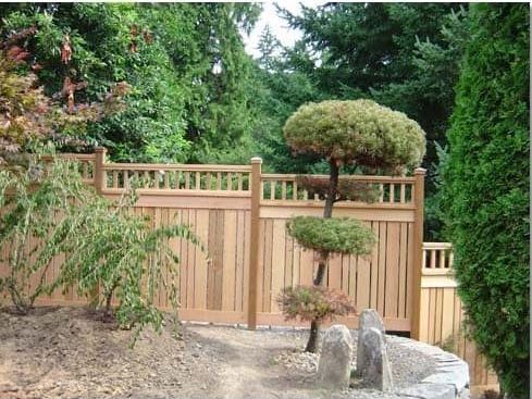 A wooden fence surrounds a garden with trees and rocks