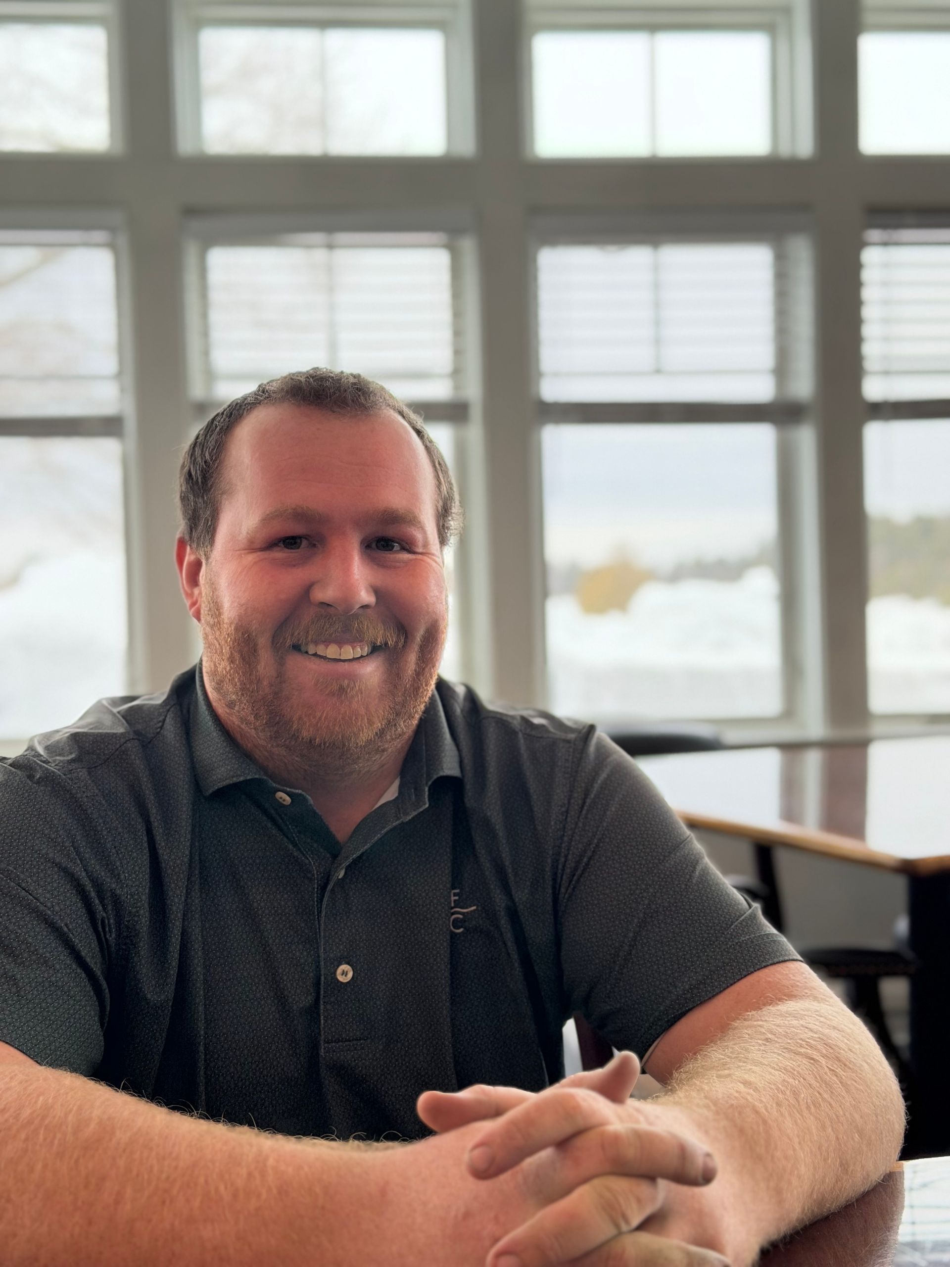 A young man in a white shirt is standing in front of a window.