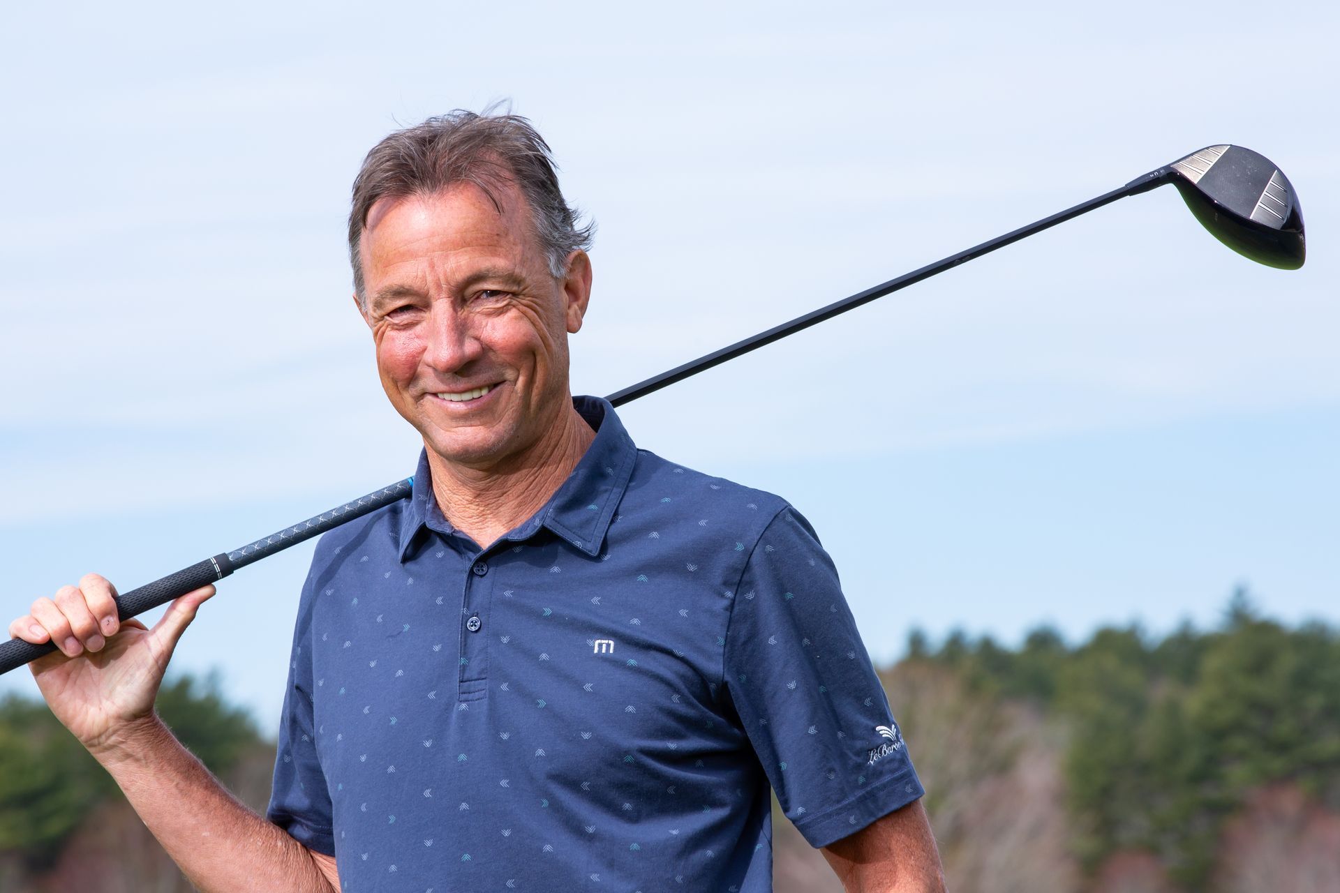 A man in a blue shirt is smiling in front of a window.