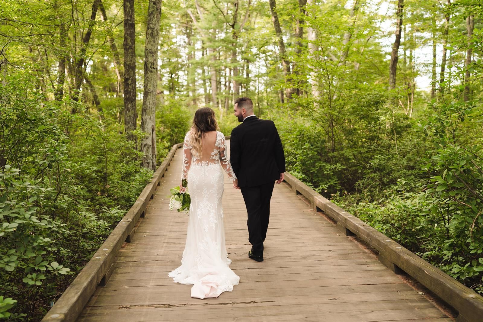 A bride and groom are walking across a wooden bridge in the woods.