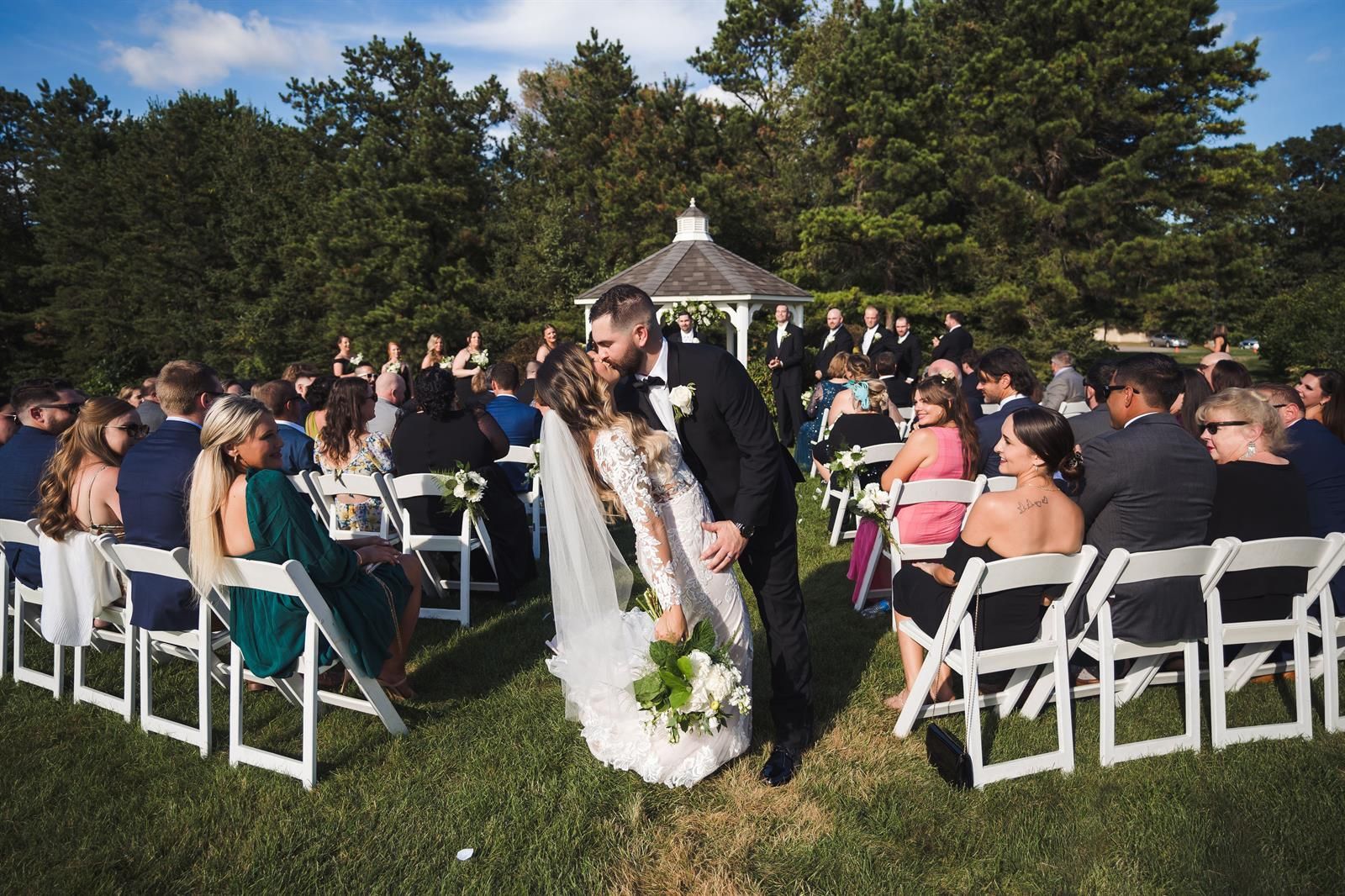 A bride and groom kissing at their wedding ceremony in front of a crowd of people.