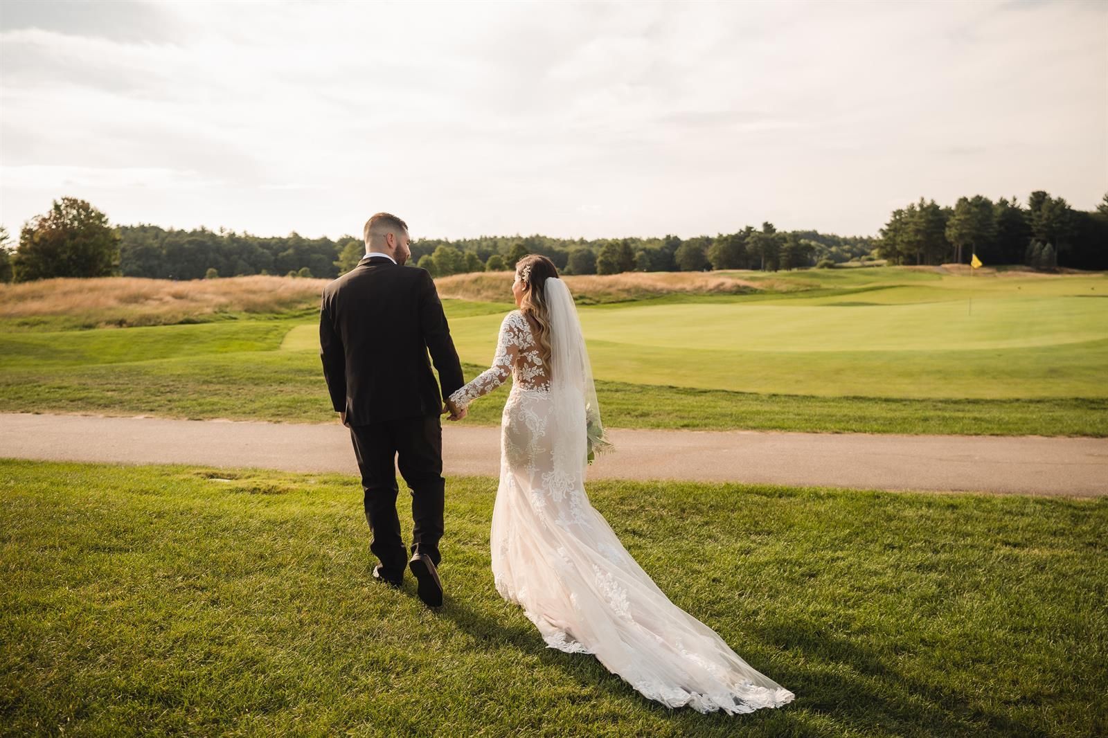 A bride and groom are walking across a golf course holding hands.
