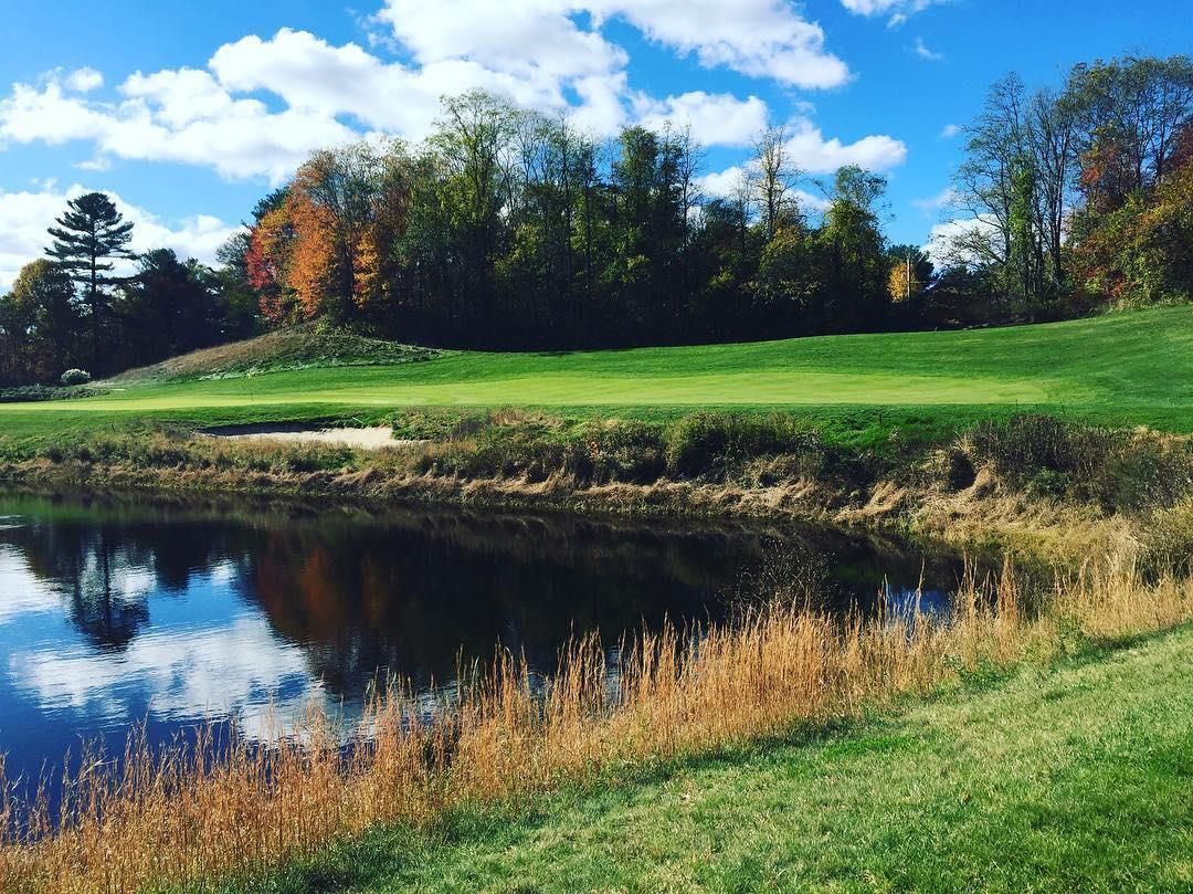 A golf course with a pond in the foreground and trees in the background.