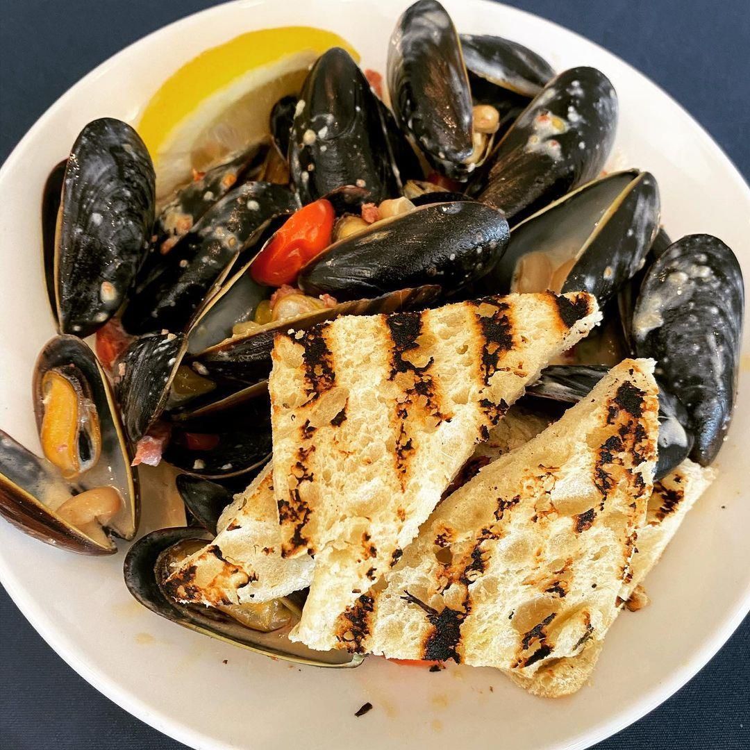 A white plate topped with mussels and bread on a table.