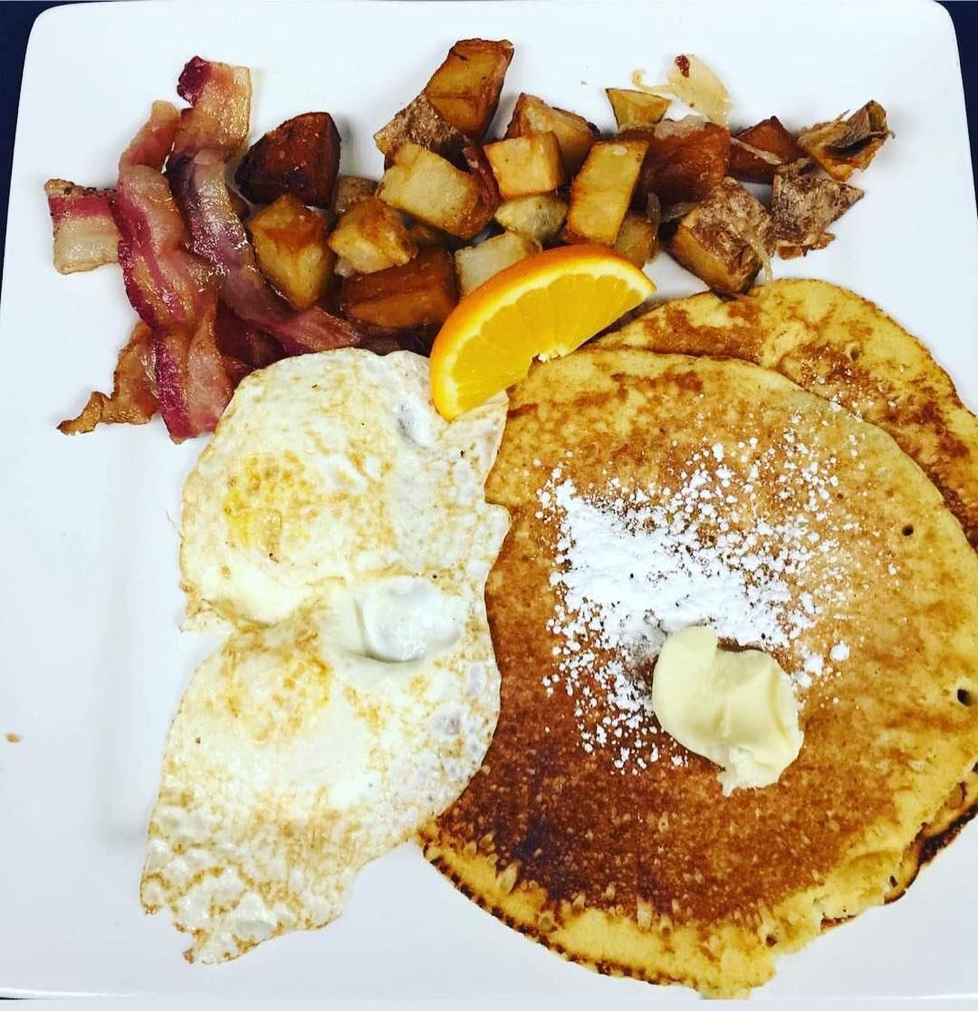 A white plate topped with pancakes eggs bacon and potatoes
