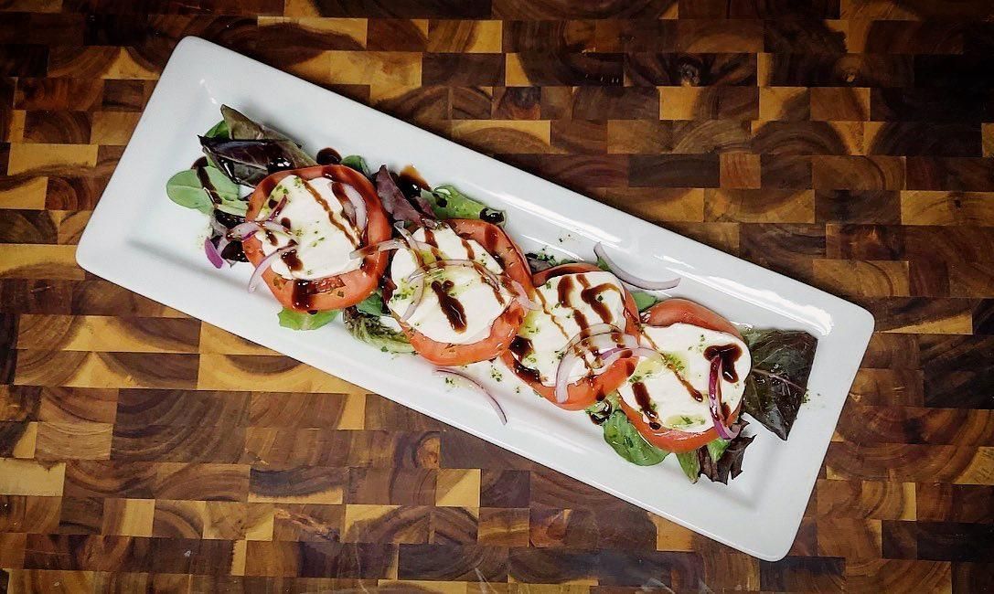 A long white plate topped with tomatoes and mozzarella on a wooden table.