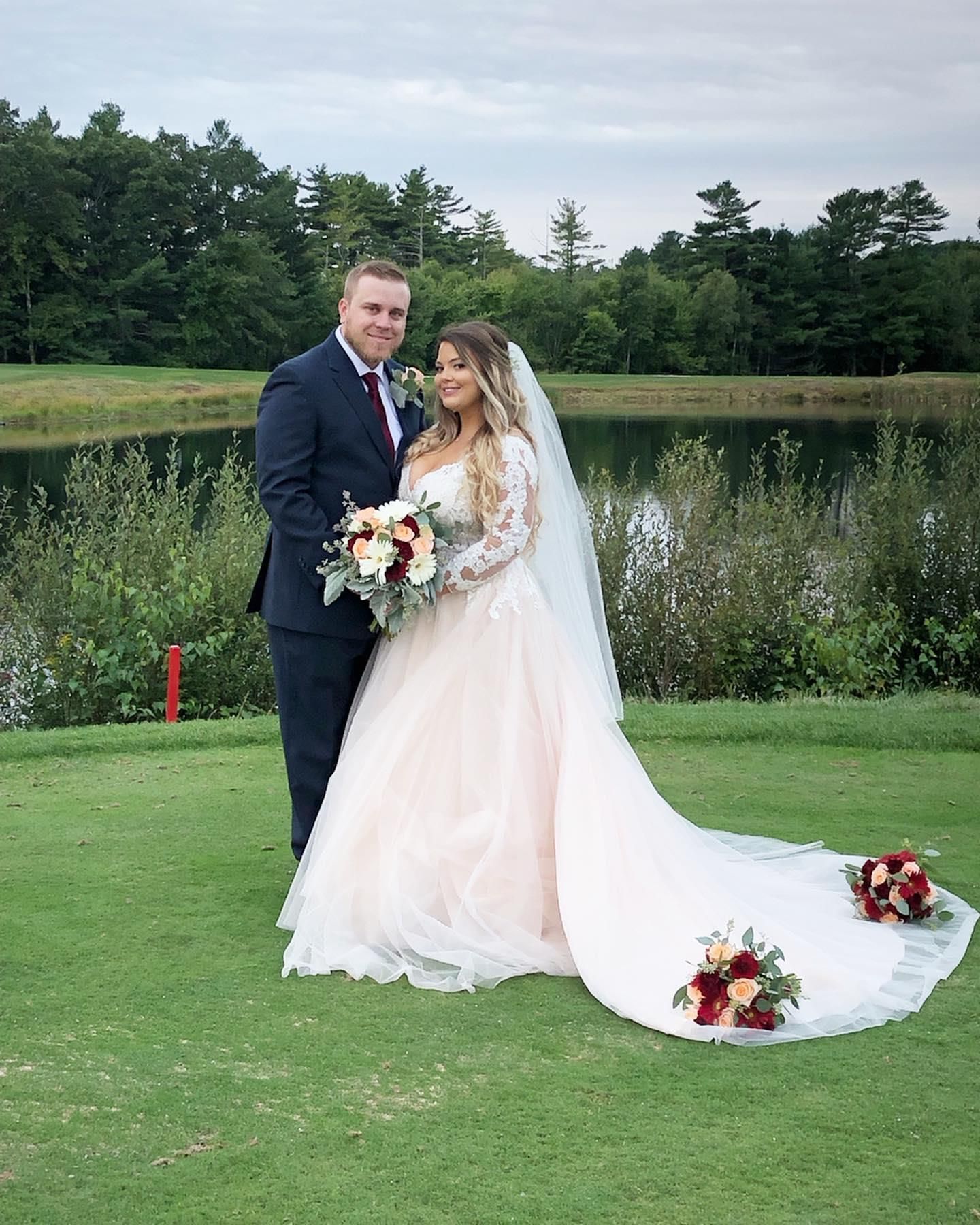 A bride and groom are posing for a picture on their wedding day in front of a lake.