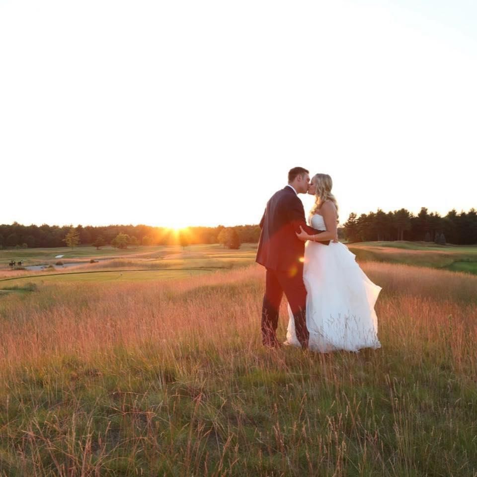 A bride and groom are kissing in a field at sunset.