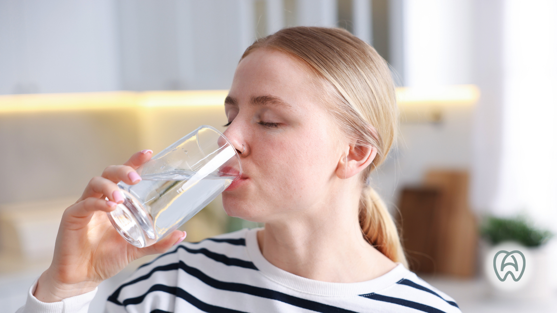 Woman drinks water from a glass; indoors.