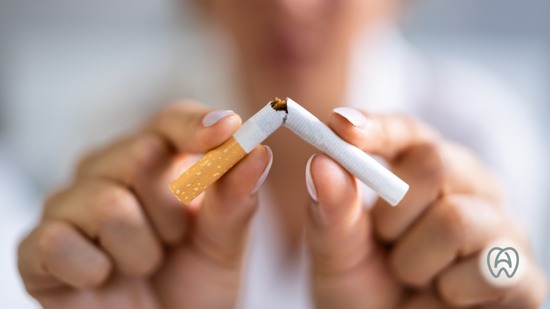 Person breaking a cigarette in half, white shirt, blurry background.