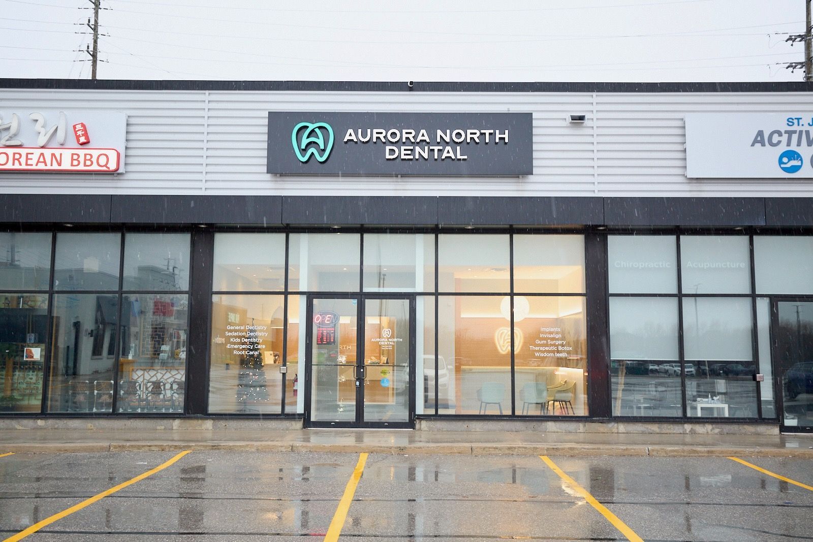 Exterior of Aurora North Dental with storefront and parking lot in the rain.
