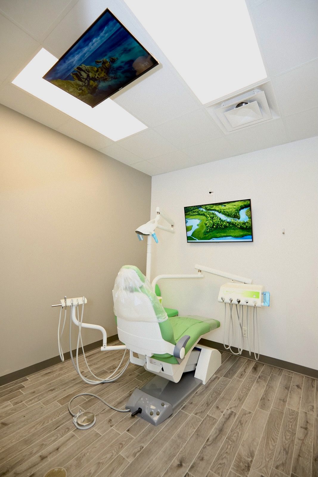 Dental chair in a light, modern room with two screens displaying nature scenes.
