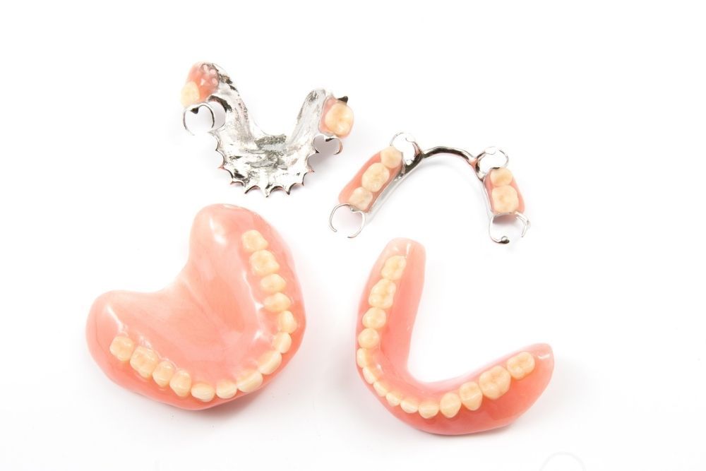 Dentures: full upper and lower sets and two partial dentures with pink gums and white teeth, on a white background.