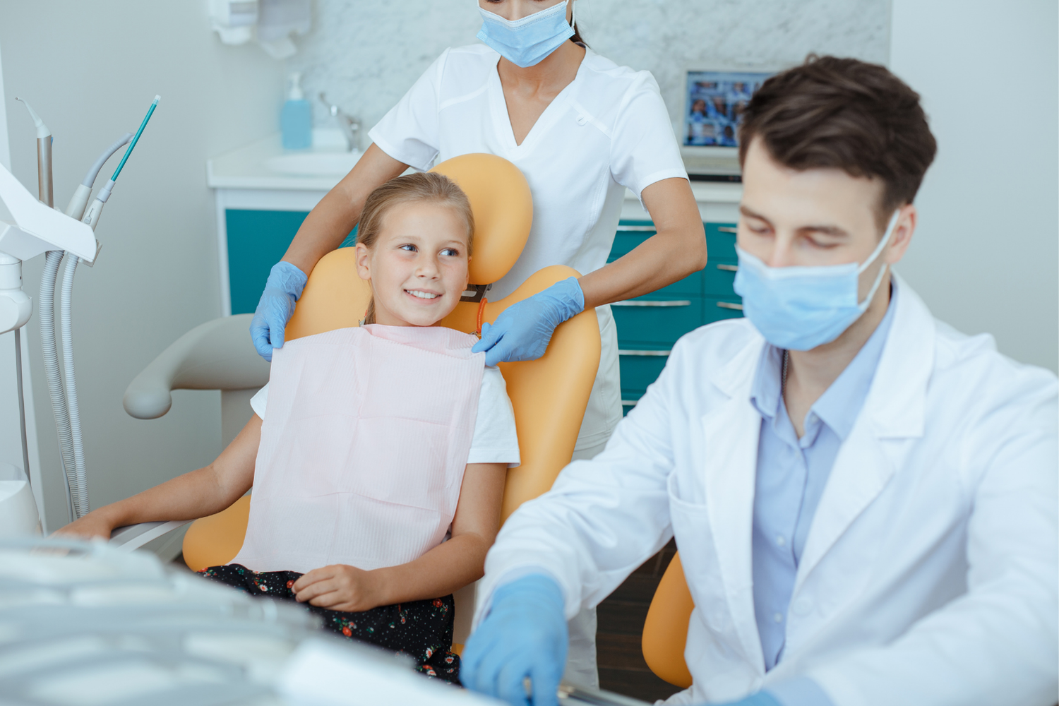 Girl in dentist chair with dentist and assistant; dental exam setting.