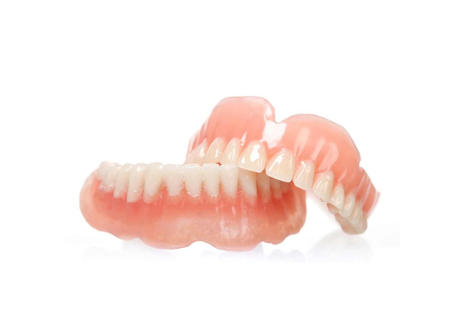 Set of dentures, upper and lower, resting on a white surface. Pink gums, white teeth.