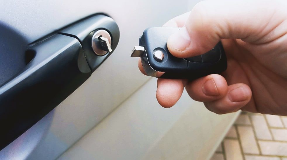 A Car Locksmith Is Holding A Car Key In Front Of A Car Door.