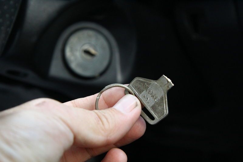 An Automotive Locksmith Is Holding A Key In Front Of A Car Ignition.