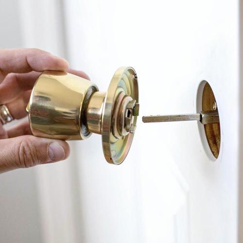 A Technician Installing A Gold Knob Lock On A Residential Door.