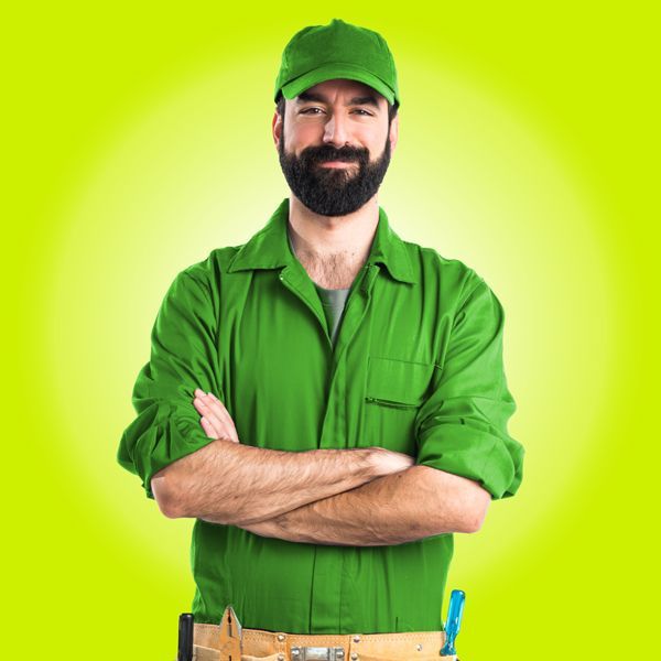 A Locksmith In A Green Uniform And A Hat Is Standing With His Arms Crossed.