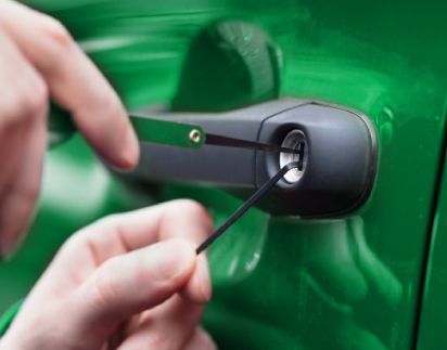 A Locksmith Is Using Picks To Open A Green Car Door.