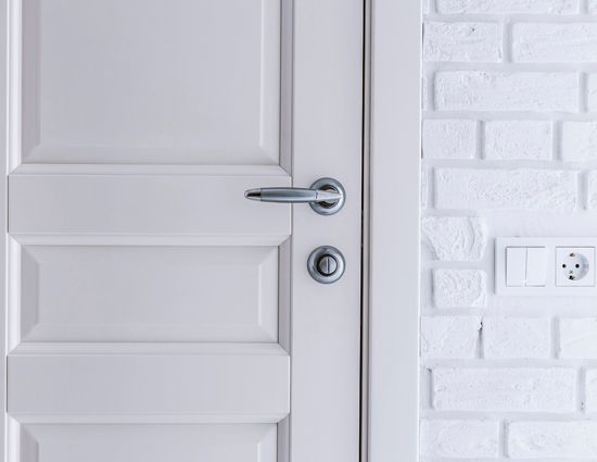 A White Door With A Silver Handle Is Next To A White Brick Wall.