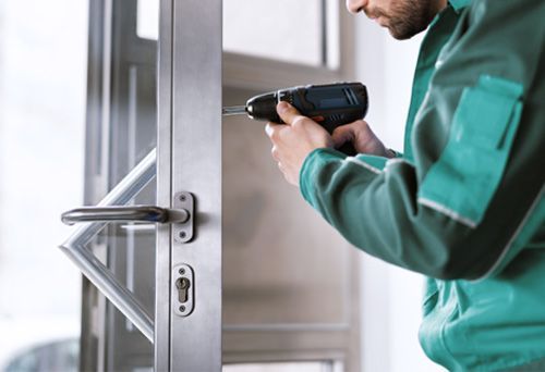 A Commercial Locksmith Is Using a Power Drill To Install a Hinged Door Lock.