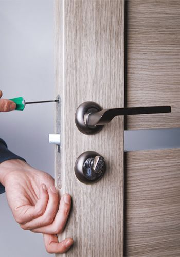 A Commercial Locksmith Is Installing A Lever Handle Lock On A Wooden Door.