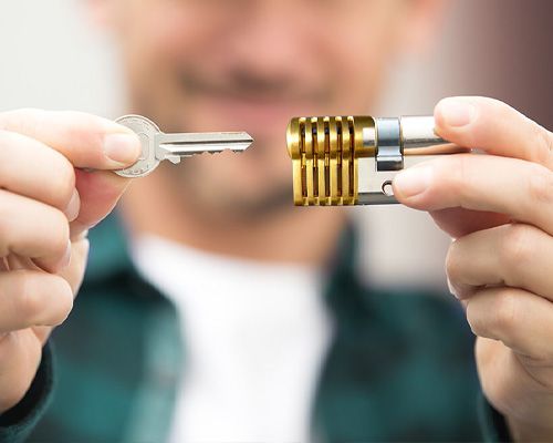 A Locksmith Technician Holds A Metal Key And Lock Cylinder In His Hands.