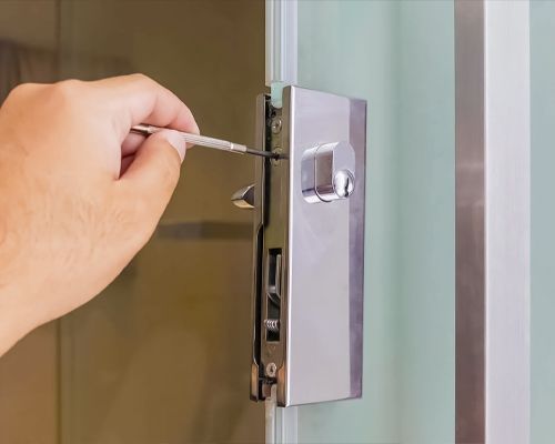 A Locksmith Is Using A Screwdriver To Repair A Silver Lock On The Door.