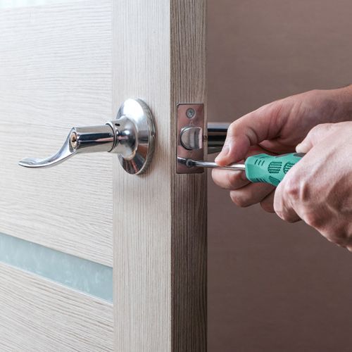 A House Locksmith Is Installing A Lever Handle Lock On A Wooden Door. 