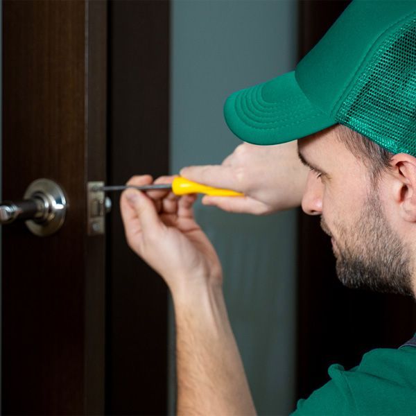 A Locksmith Is Using A Screwdriver To Install A Lever lock On A Dark Wooden Door.