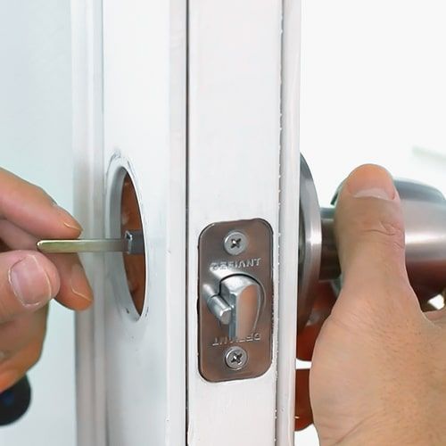 A Locksmith Is Installing A Doorknob On A White Door.