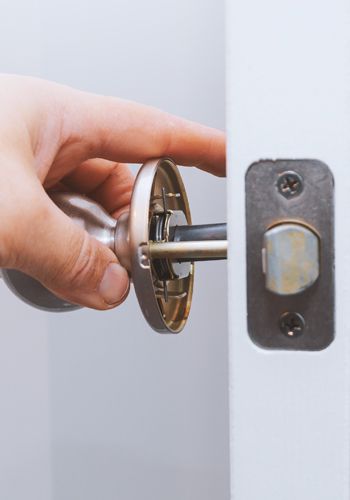 A Technician Is Fixing A Doorknob Lock On A White Door.