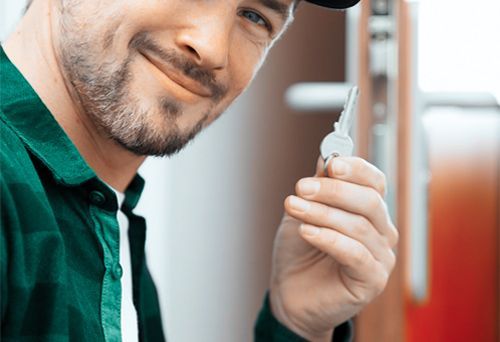 A Technician Is Smiling As He Holds A Metal Key Between His Fingers.