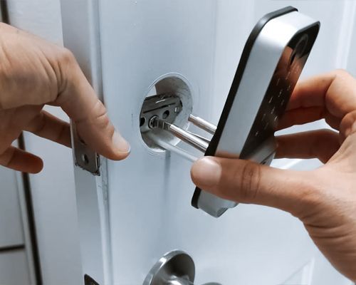 A Technician Is Installing A Smart Lock In A White Door Of A House.