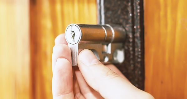 A Technician Is Inserting A Silver Cylinder Lock On A Wooden Door.