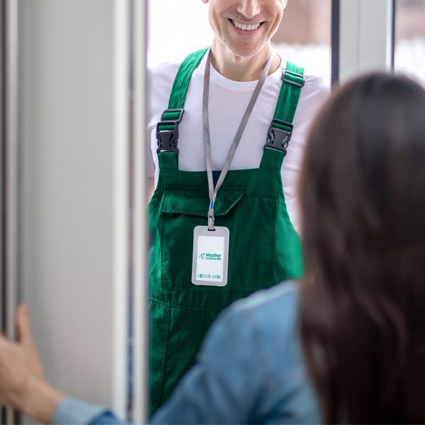 A Locksmith In Green Overalls Arrives To Provide Mobile Locksmith Services At The Door Of A Lady's Home.