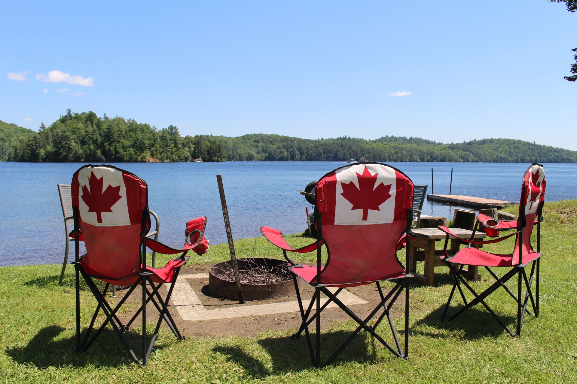 A group of chairs with canadian flags on them are sitting around a fire pit.