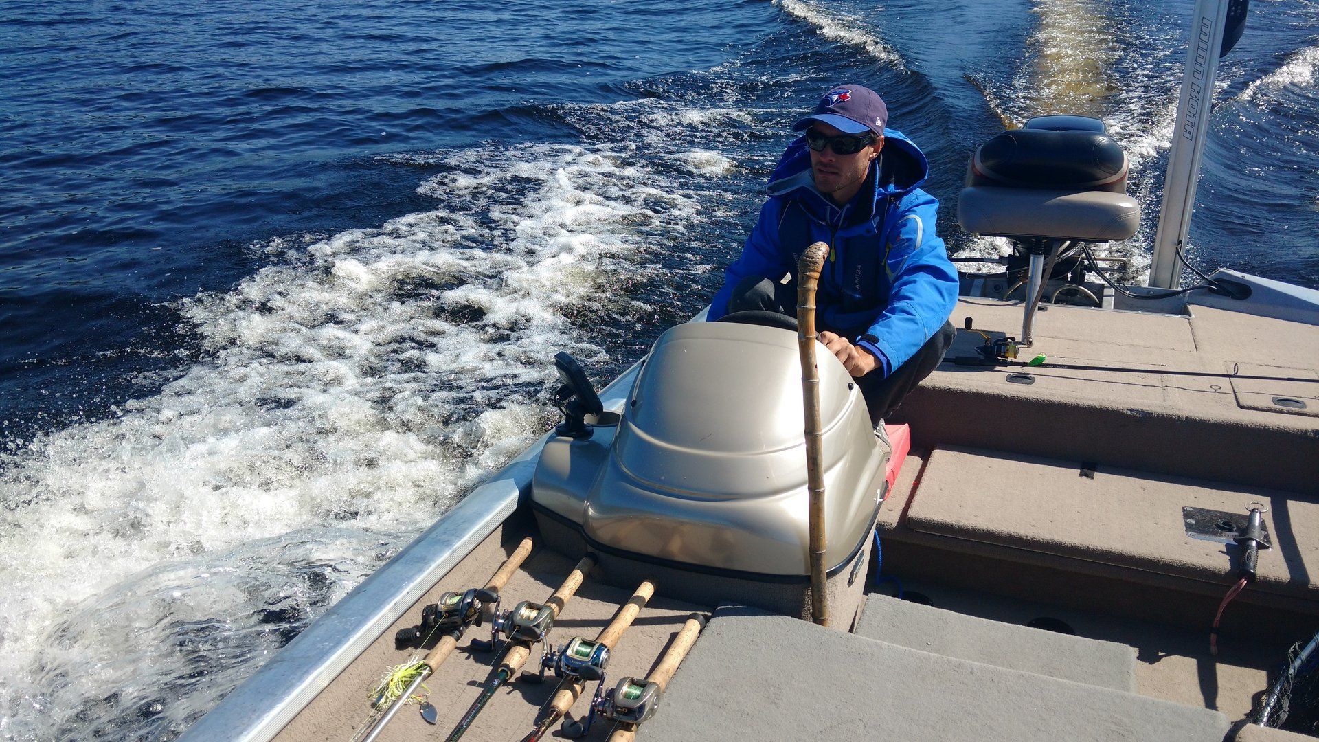 A man is driving a boat with fishing rods on the deck