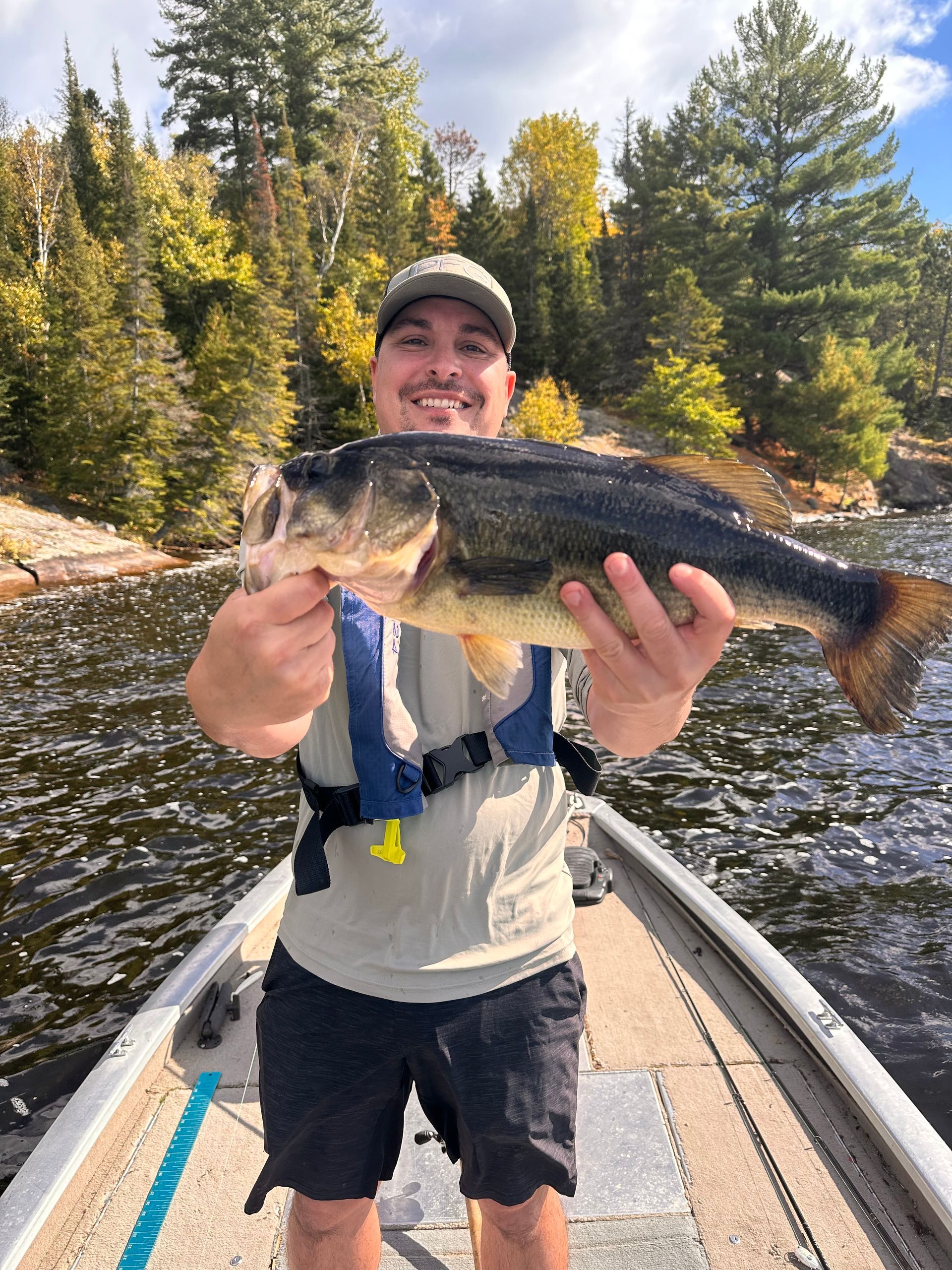 A man is standing on a boat holding a large bass.