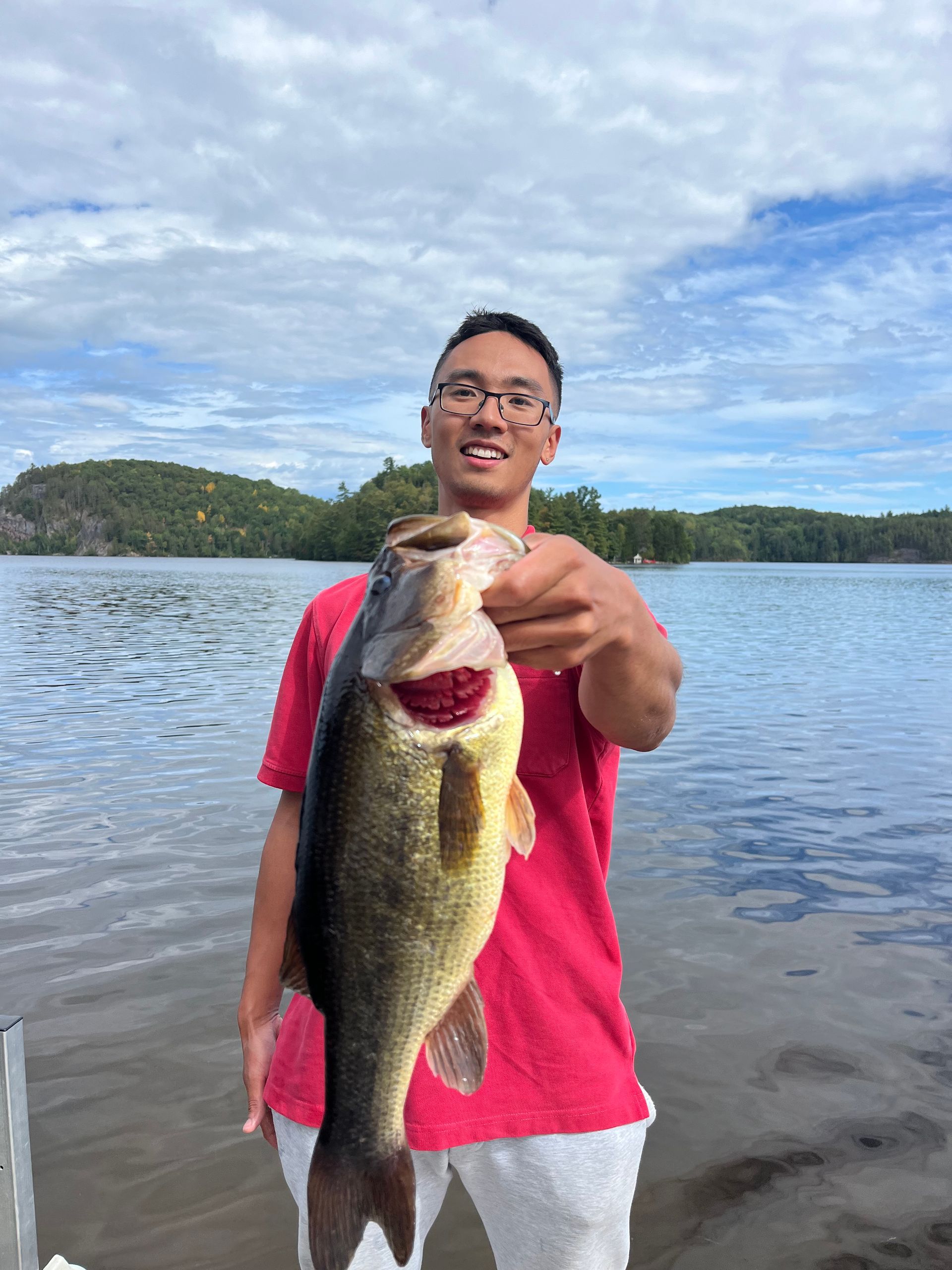 A man is holding a large fish in his hands in front of a lake.