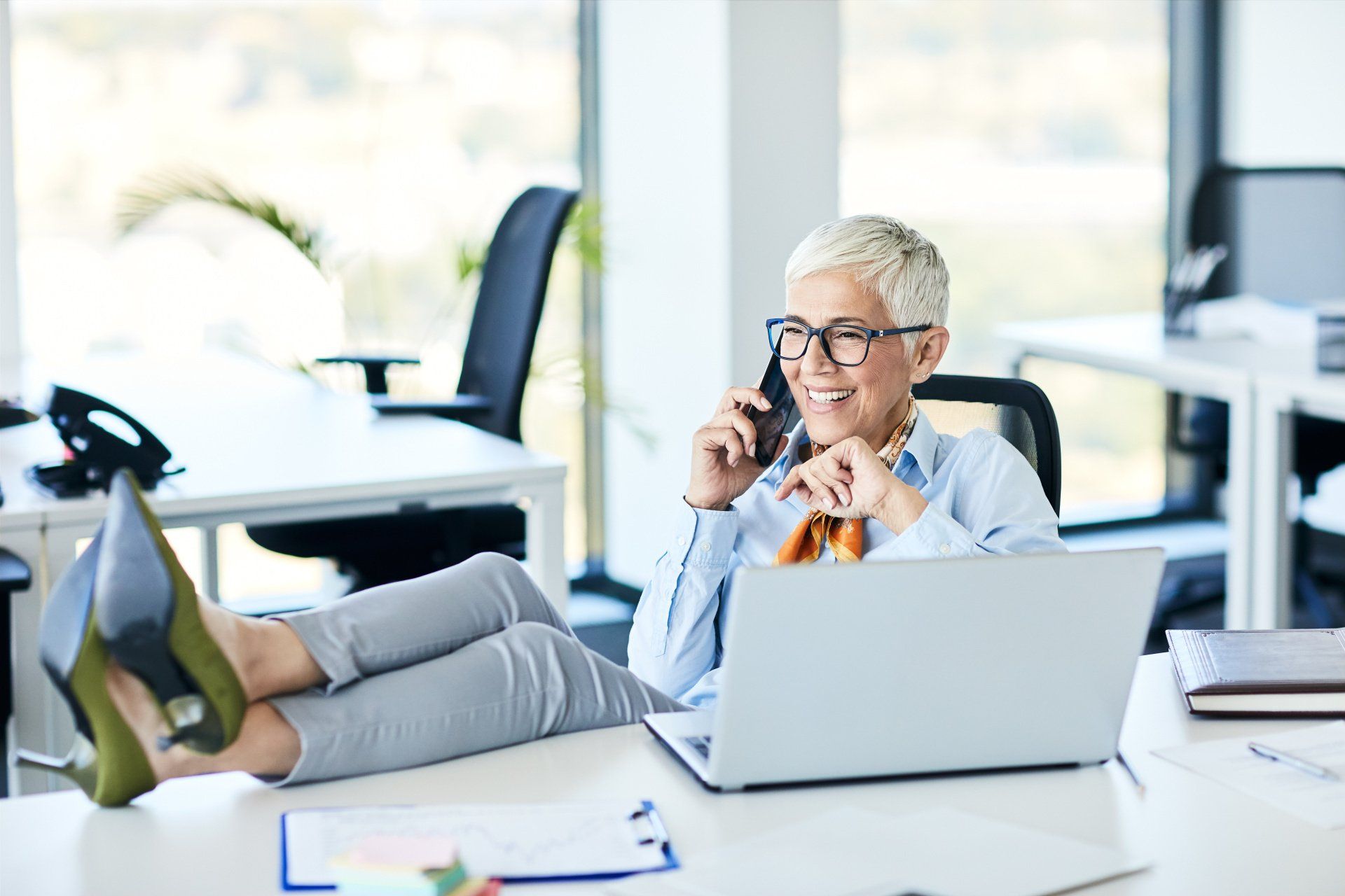 a woman is sitting at a desk with her feet up and talking on a cell phone