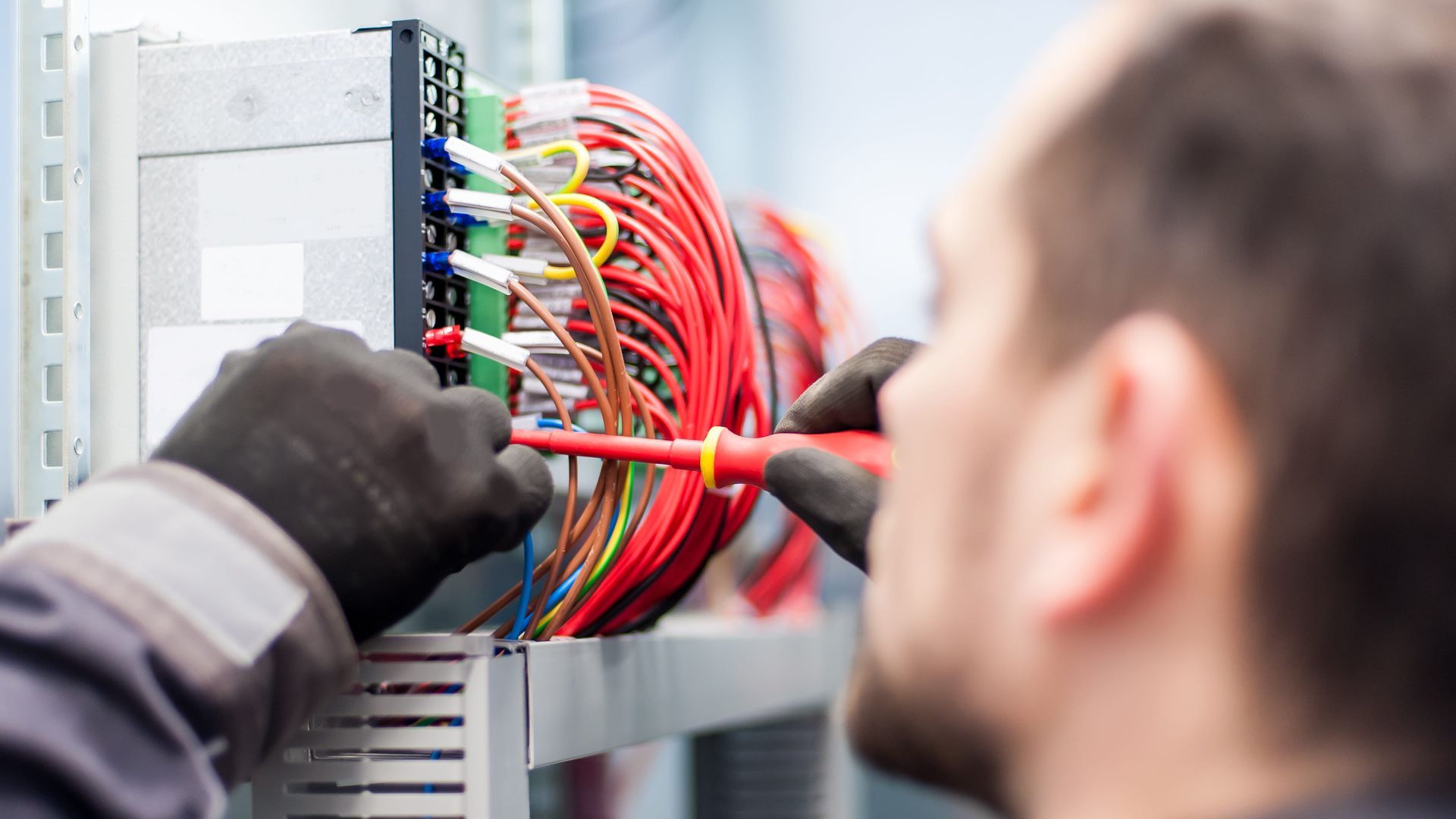 A man is working on an electrical box with a screwdriver.