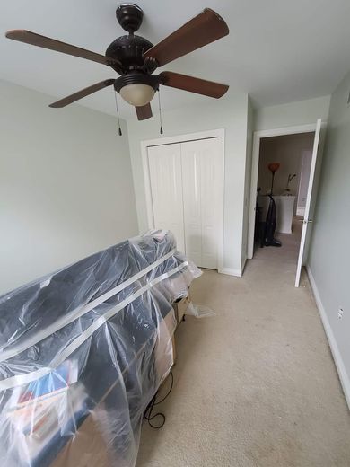Bedroom with closet, bed covered in plastic, doorway to a bathroom; ceiling fan.